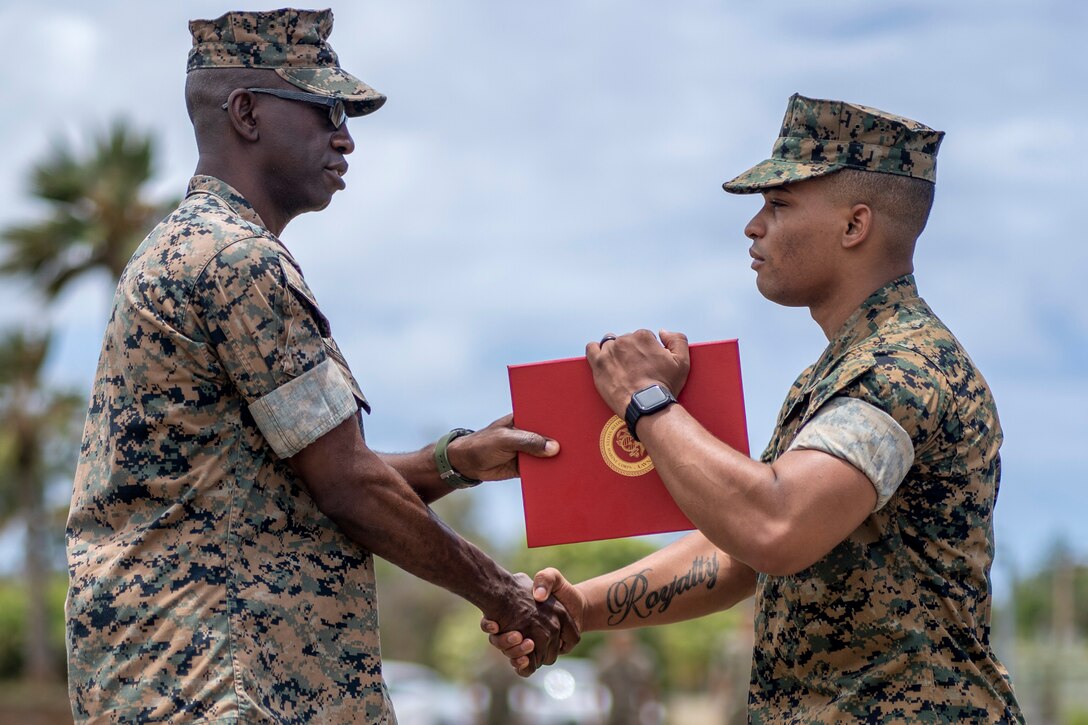 Two Marines shake hands as one passes a certificate to the other.