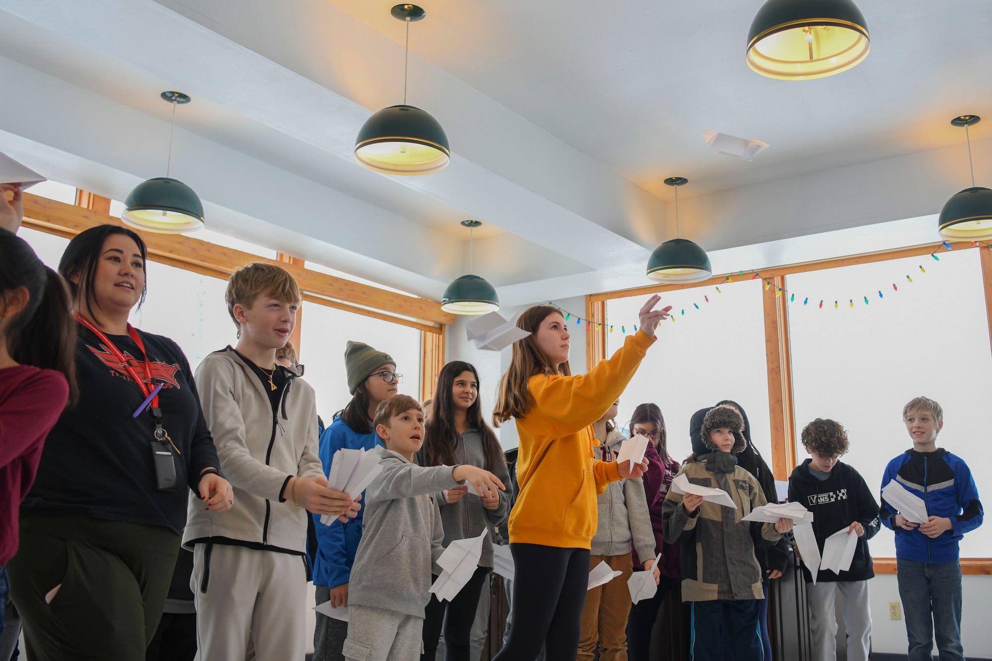 Several young children throw paper airplanes across a windowed white room in winter