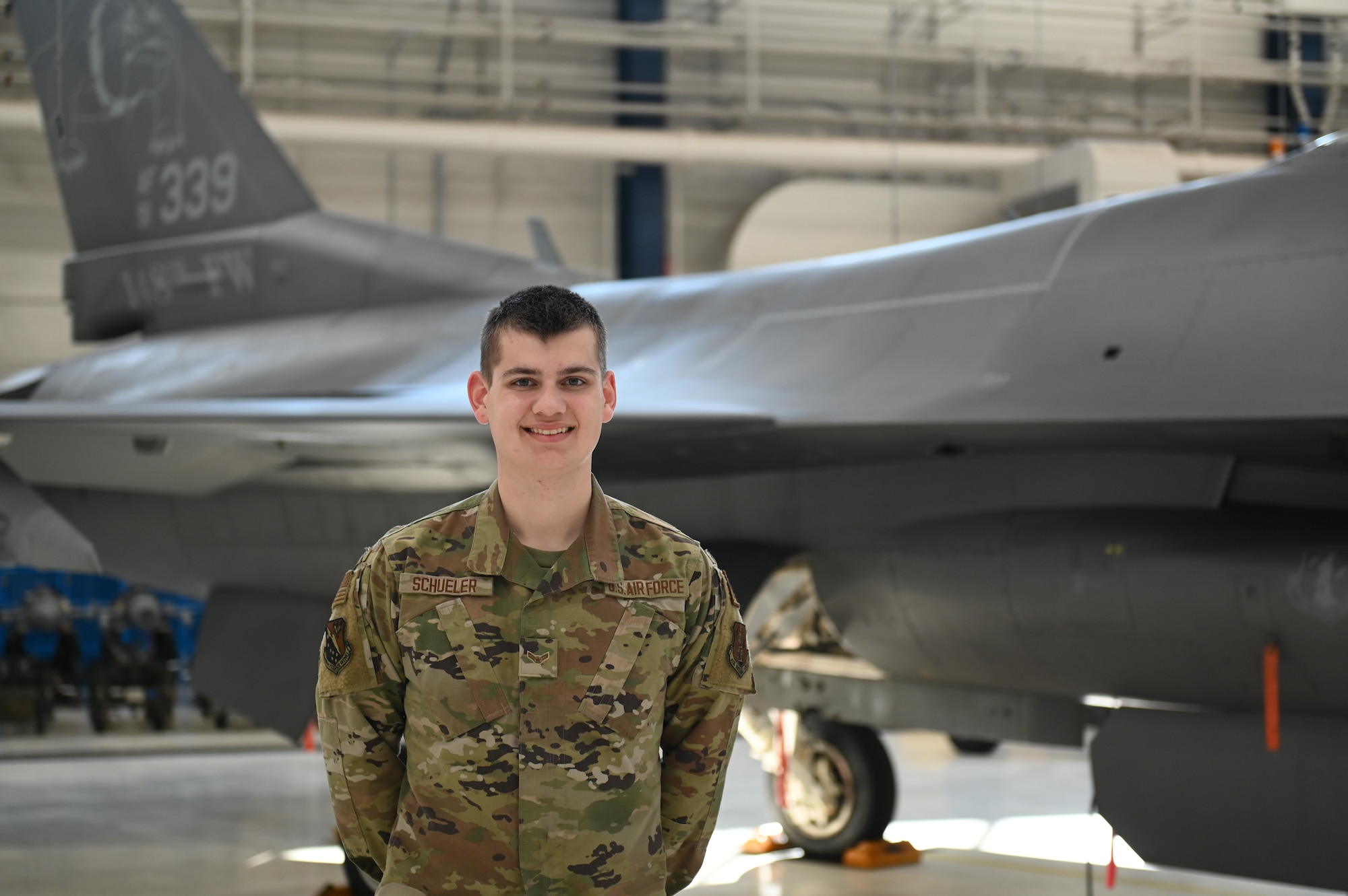 U.S. Air National Guard tactical aircraft maintenance specialist, Airman 1st Class Ayden Schueler, poses for a photo in front of an F-16 Fighting Falcon assigned to the 148th Fighter Wing, Minnesota Air National Guard, on February 24, 2023. Schueler is one of seven airmen assigned to the 148th Fighter Wing who earned the highest possible ASVAB AFQT score of 99.