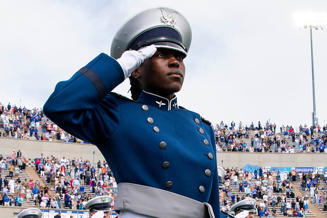 A cadet salutes on the field of a packed stadium.