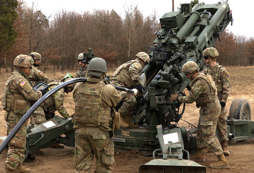 Uniformed people operate a large gun.