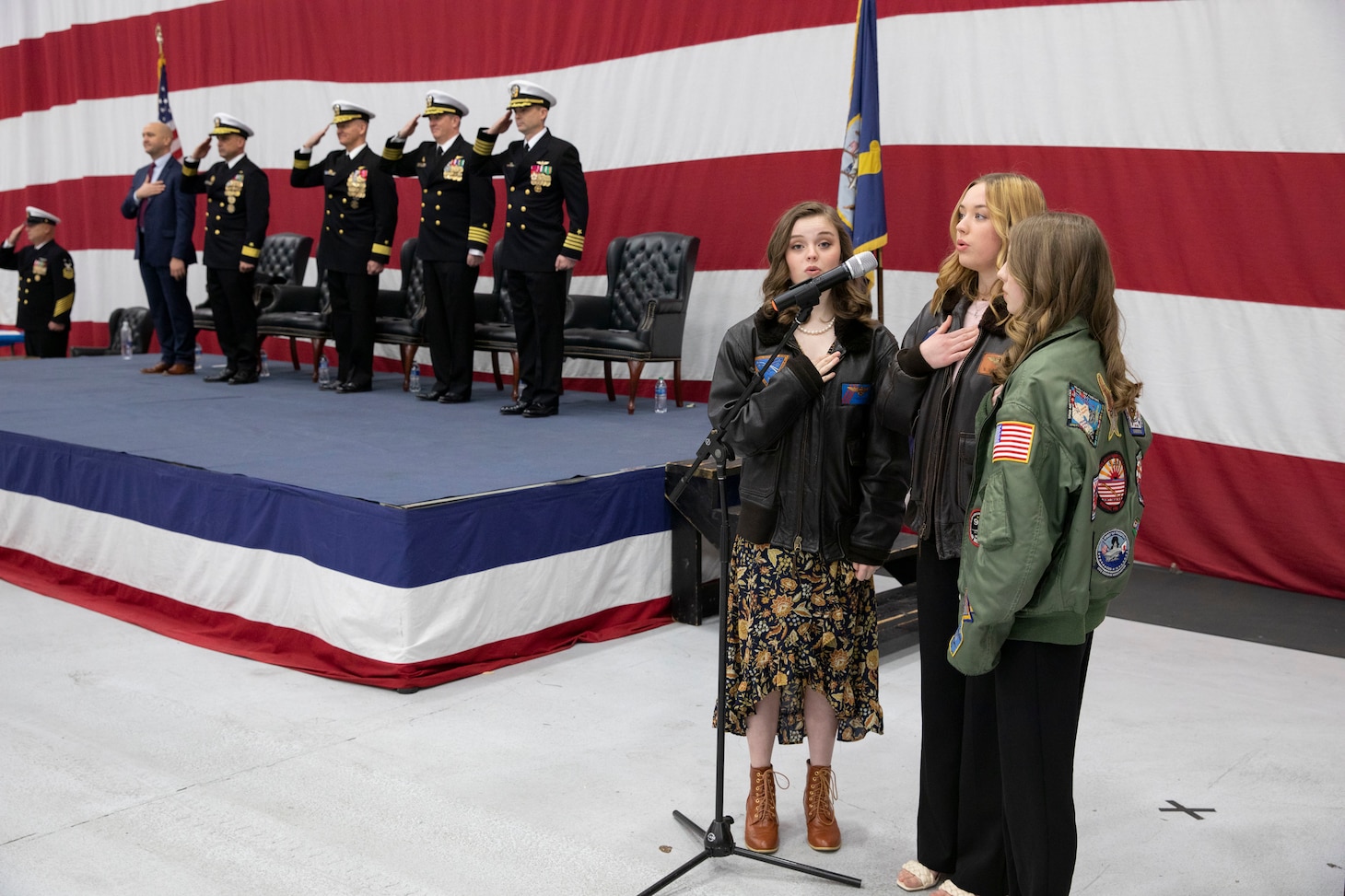 May, Emily and Molly Fraser, daughters of Capt. William Fraser, outgoing Commander, Tactical Support Wing (CTSW), sing the national anthem during the CTSW change of command ceremony in the Fleet Logistics Support Wing (VR) 59 hangar at Naval Air Station Joint Reserve Base Fort Worth, Texas.