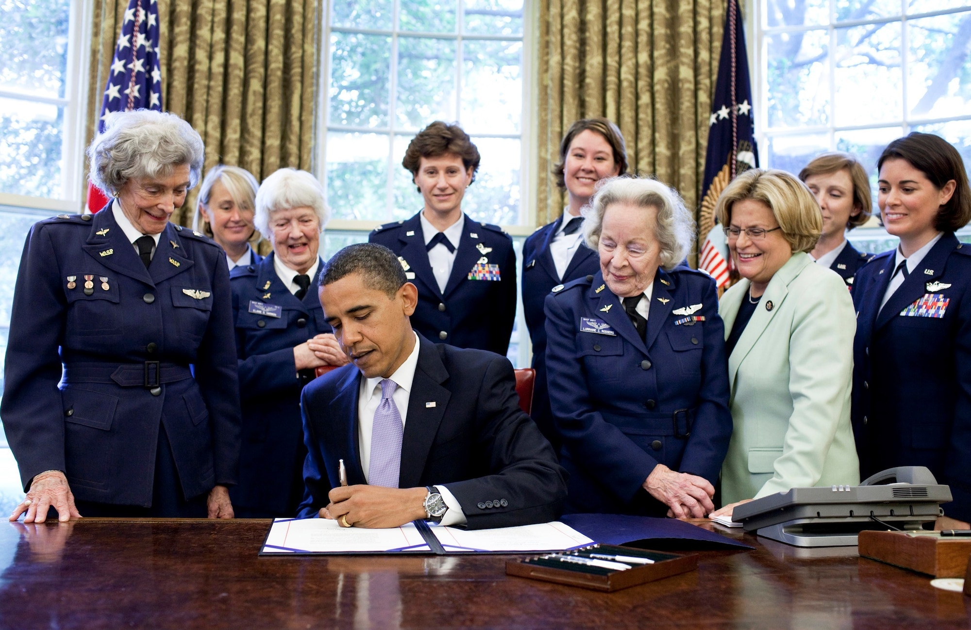 Pres. Barack Obama signs a bill at his desk at the White House with female advocates for the Women Airforce Service Pilot corps looking on.