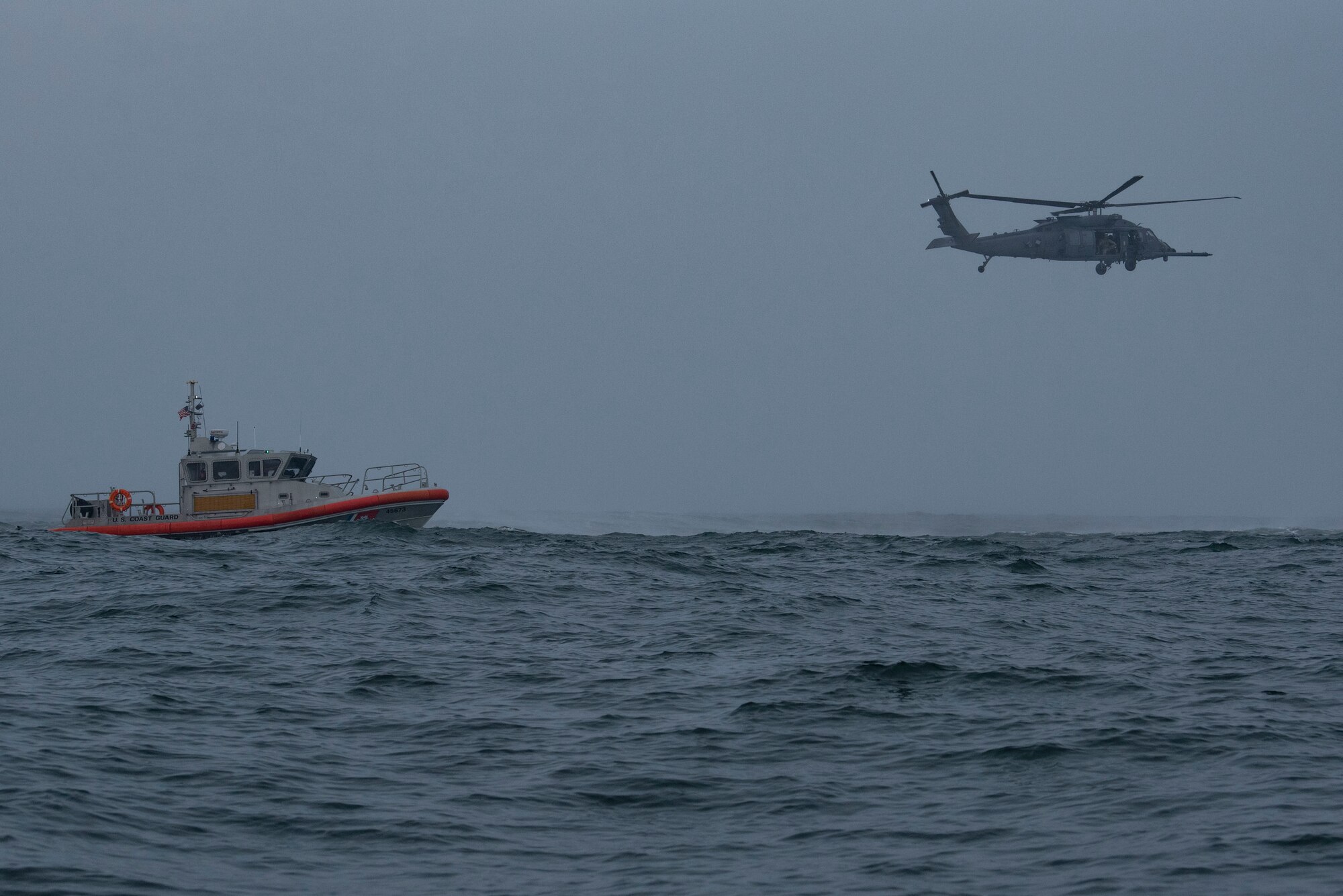 HH-60W Jolly Green II helicopter prepares for a hoist operation near a U.S. Coast Guard 45-foot response boat