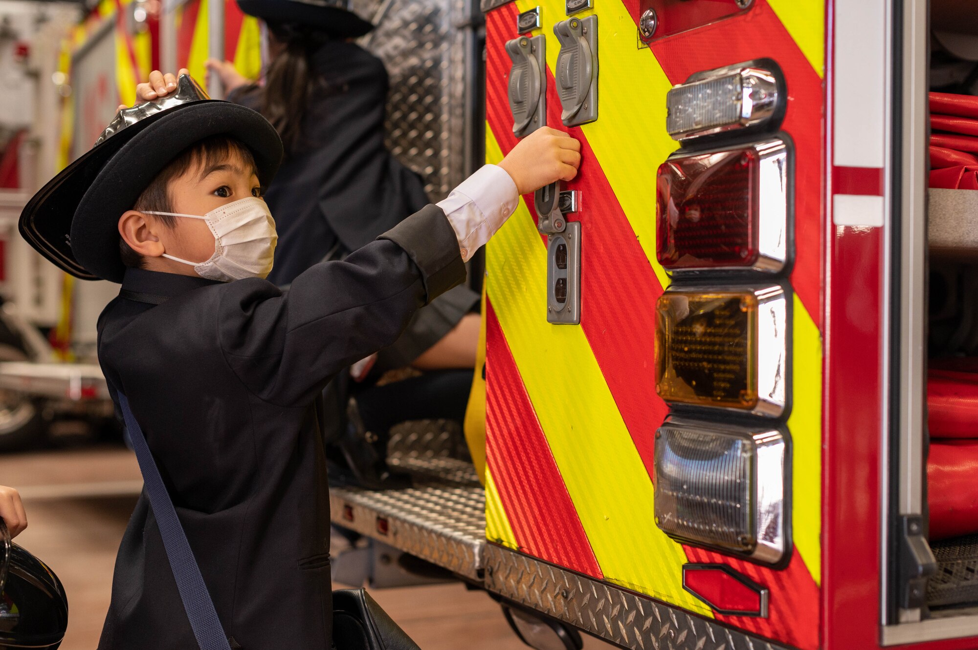 A Japanese child climbs onto a fire truck.