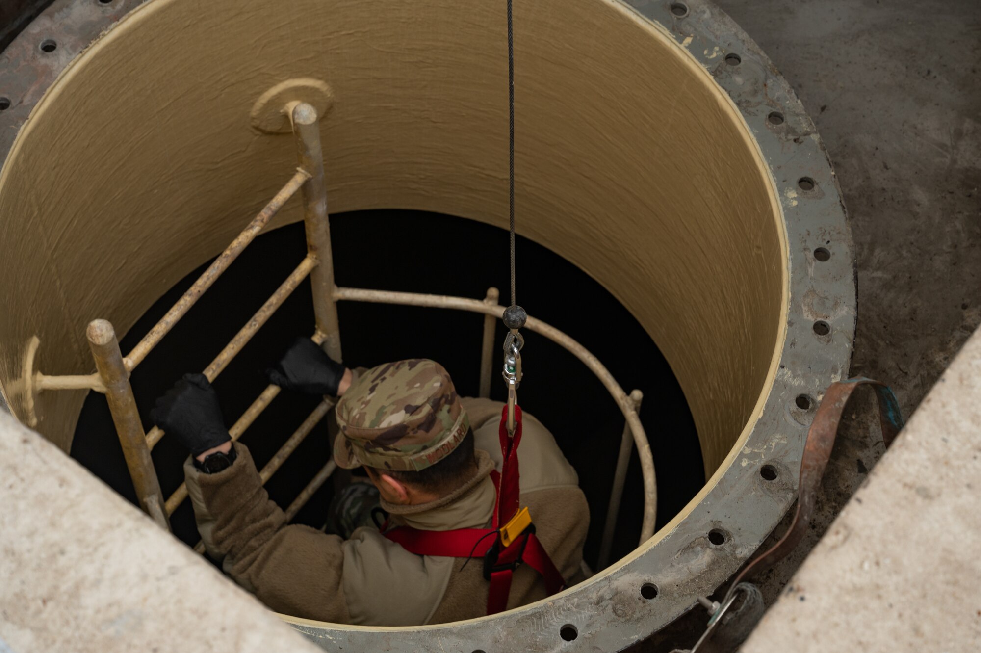 U.S. Air Force Lt. Col. Christopher Woolard, 100th Mission Support Group deputy commander, makes his way down the ladder into an emptied jet fuel storage tank, Feb. 28, 2023, at Royal Air Force Mildenhall, England.