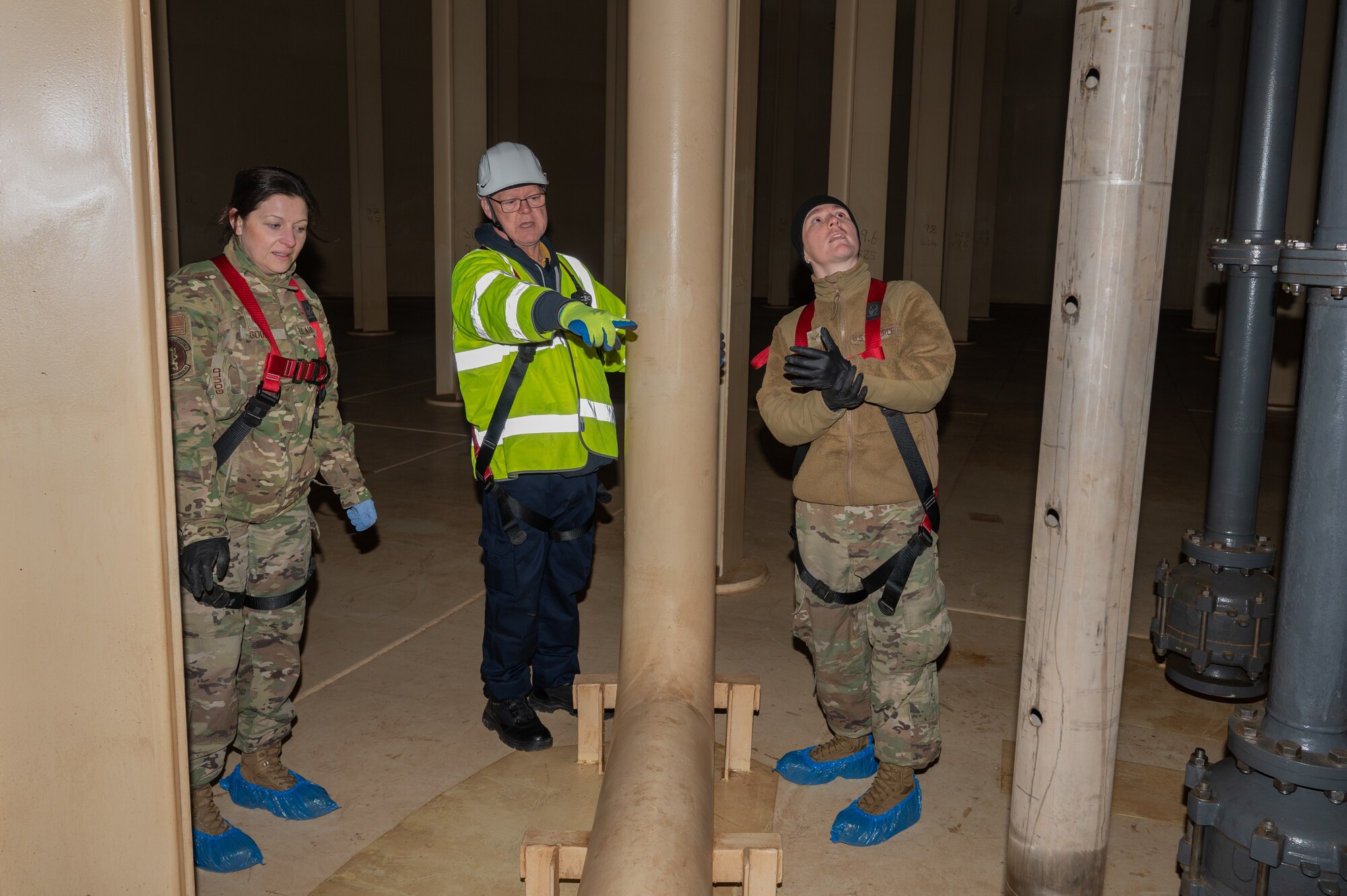 U.S. Air Force Tech. Sgt. Elizabeth Gould, left, 100th Logistics Readiness Squadron household goods NCO in charge, Senior Airman Austin Alvarado, right, 100th LRS fuels distribution operator, and Gladstone “Jock” Breckney, middle, Environmental Chemical Corporation project manager, talk in the center of the drained jet fuel storage tank, Feb. 28, 2023, at Royal Air Force Mildenhall, England.