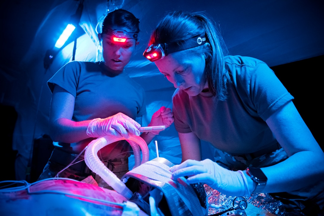 Two airmen wearing headlamps lean over a simulated patient.