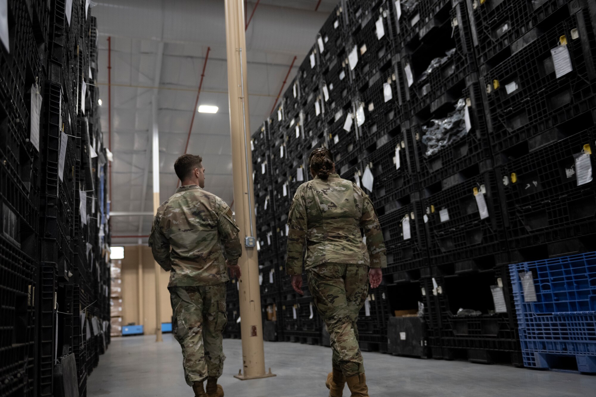 A photo of two people walking through an isle of stacked black storage boxes.