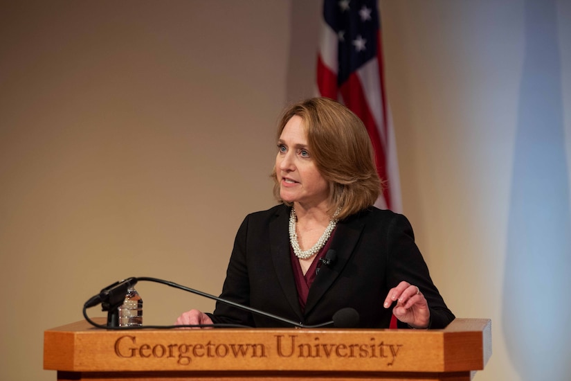 A woman is shown from the chest up, speaking behind a podium.