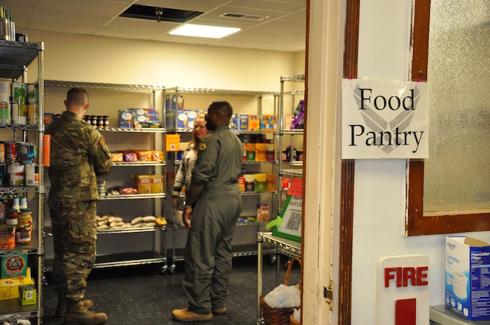 Two men and one woman stand in a room surrounded by metal shelves with food