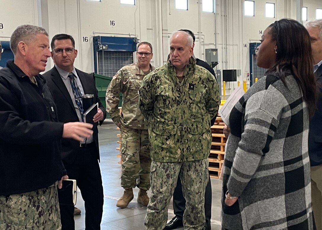Man in a camo uniform talks to a woman with four  men standing by.