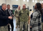 Man in a camo uniform talks to a woman with four  men standing by.