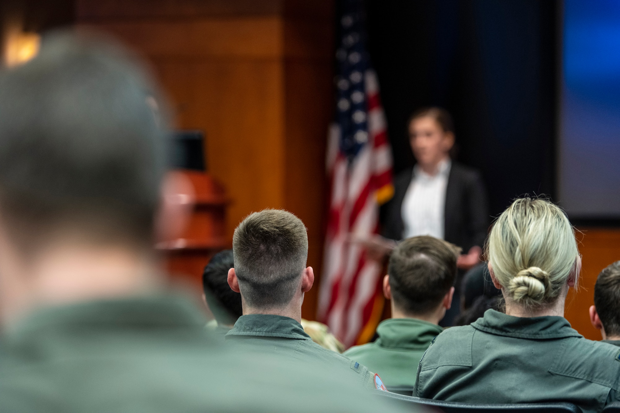 A person stands at the front of an audience of military people.