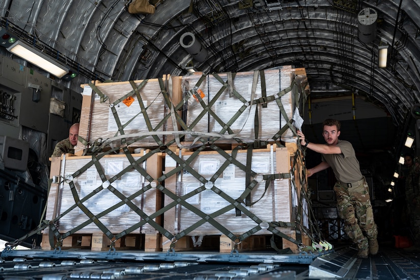 An airman slides large pallets of cargo onto an aircraft.