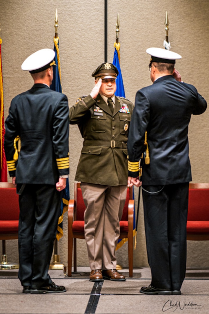 Three men in military uniform salute and pose during a change of command ceremony.