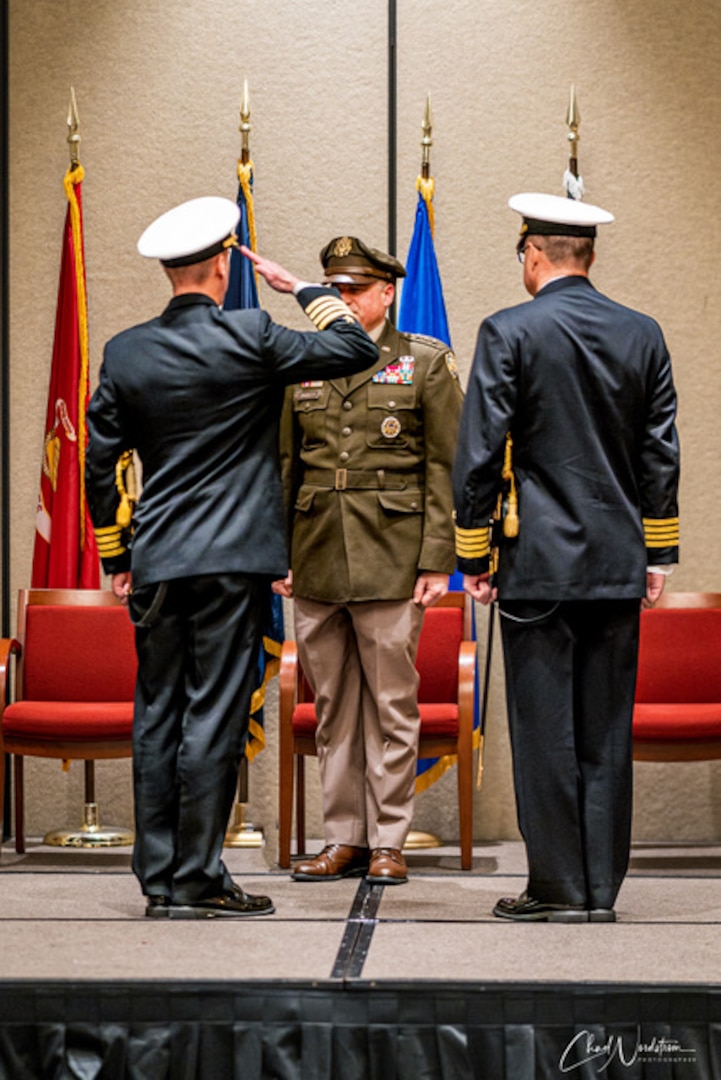 Three men in military uniform salute and pose during a change of command ceremony.
