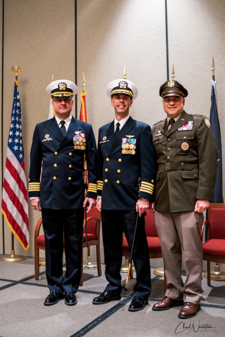 Three men in military uniform salute and pose during a change of command ceremony.