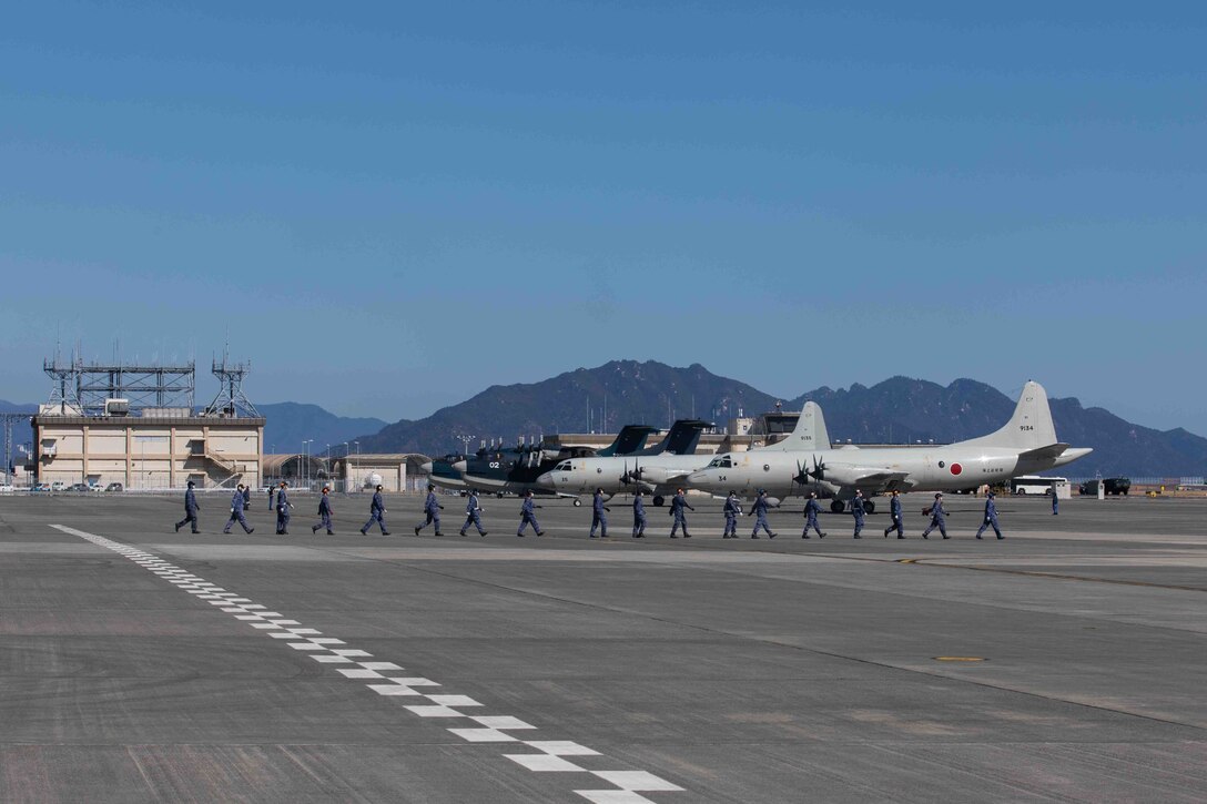 2022年2月27日に米海兵隊岩国航空基地で実施された能力デモンストレーションにおいて、参加する航空機を誘導するためにフライトラインを横切って歩く海上自衛隊員。このデモンストレーションには、米海兵隊岩国航空基地司令部司令中隊（H&HS）所属の米海兵隊UC-12Wヒューロン、第1海兵航空団第12海兵飛行大隊（MAG-12）所属のF-35ライトニングII（2機）とKC-130Jスーパーハーキュリーズ、第5空母打撃群（CSG-5）第5空母航空団（CAW-5）所属の米海軍F/A-18Eスーパーホーネット（3機）、F/A-18Fスーパーホーネット、EA-18Gグラウラー、E-2ホークアイ、C-2グレイハウンド、第31航空群（FAW-31）所属の海上自衛隊US-2、EP-3、OP-3C、UP-3D、U-36A、MCH-101が参加し、日米同盟と自由で開かれたインド太平洋地域を支援するハイレベルな即応態勢と複合能力を示した。米海兵隊岩国航空基地は、併設された港湾施設と飛行場を使用し、岩国基地以外の所属航空機を運用する中継地や様々な作戦活動のための中継地として機能することで、統合軍を支援する能力を有している。（写真：ダリエン・ライト伍長）