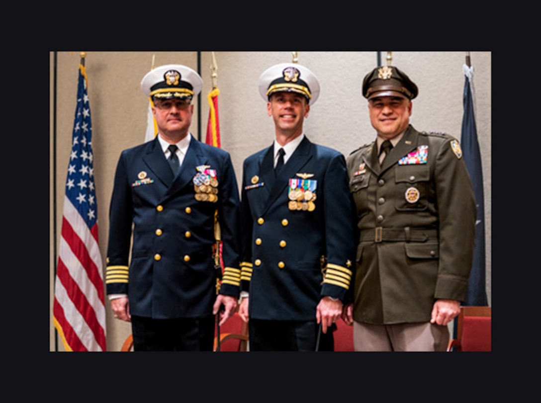 Three men in military uniform salute and pose during a change of command ceremony.