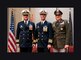 Three men in military uniform salute and pose during a change of command ceremony.