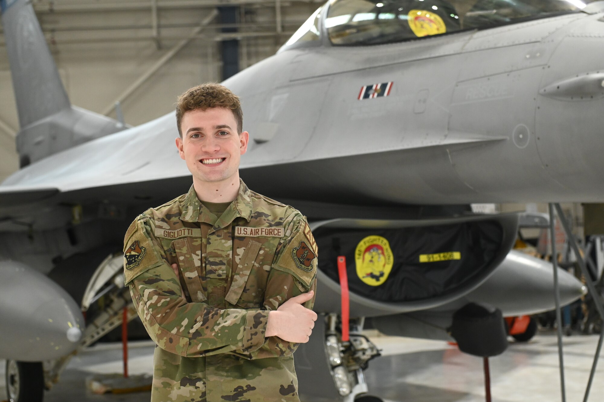 U.S. Air National Guard fighter aircraft integrated avionics specialist, Airman 1st Class Joey Gigliotti, poses for a photo in front of an F-16 Fighting Falcon assigned to the 148th Fighter Wing, Minnesota Air National Guard, on February 05, 2023. Gigliotti is one of seven airmen assigned to the 148th Fighter Wing who earned the highest possible ASVAB AFQT score of 99.
