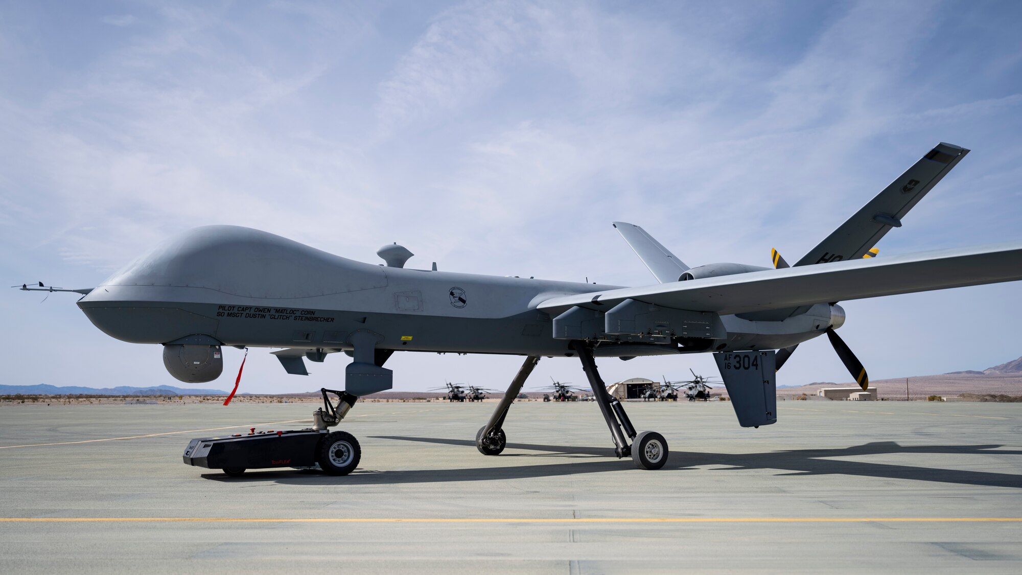 A TowFLEXX TF3 aircraft tug hauls an MQ-9 Reaper along a runway at Marine Corps Air Ground Combat Command Center, Twentynine Palms, California, Feb. 16, 2023. Agile Combat Employment Reaper 23.6 saw Airmen from Holloman Air Force Base, Cannon AFB, N.M., and Creech AFB, Nevada, participated in Agile Combat Employment Reaper 23.6 at Twentynine Palms to hone their skills while also supporting RPA training for the Marines. (U.S. Air Force photo by Staff Sgt. Kristin West)