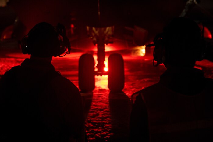 A photo of two maintenance Airmen backlit by a red light