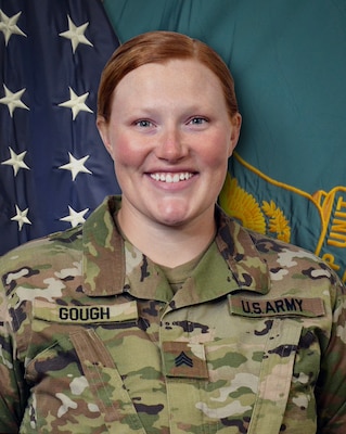 Woman in U.S. Army uniform standing in front of two flags.