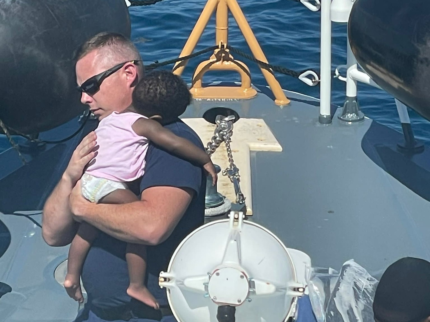 A petty officer aboard Coast Guard Cutter Manowar holds a Haitian baby, Feb. 28, 2023 off Florida's coast. The people were repatriated to Haiti on March 3, 2023. (U.S. Coast Guard photo by Senior Chief Petty Officer Brodie MacDonald)