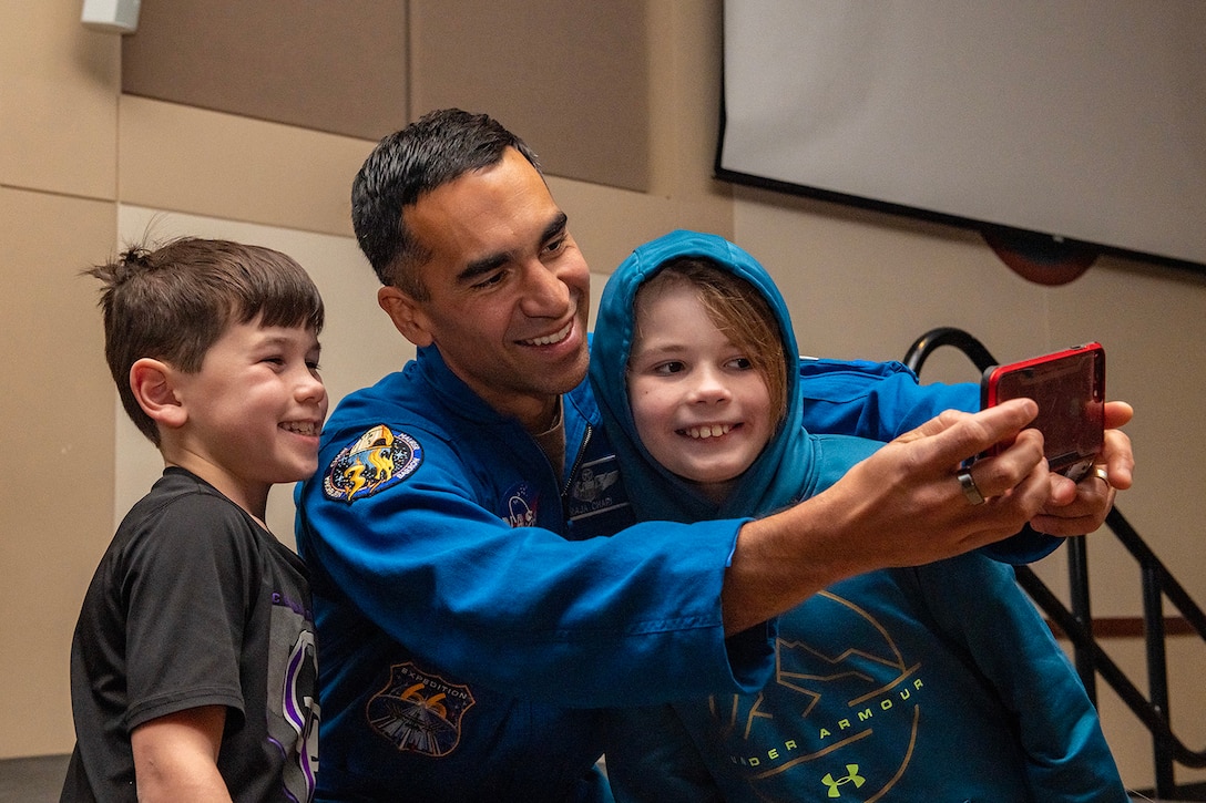 An airman and two children smile as they take a selfie photo.