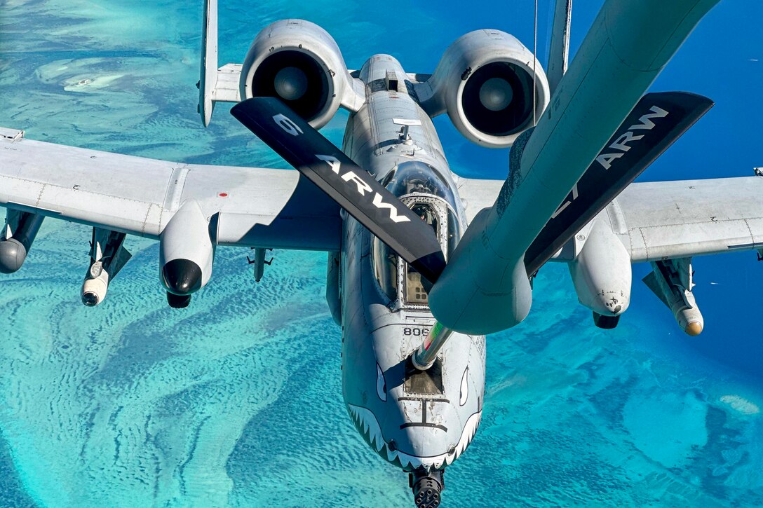 An aircraft receives fuel from another aircraft while flying over a body of water.