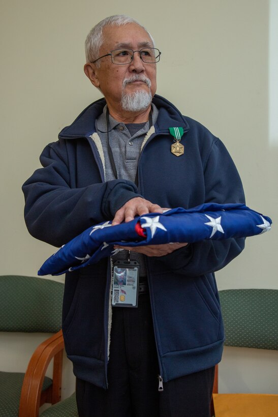 Dan Corte-Real, regional project manager for the Consolidated Storage Program, II MEF Logistics Command, holds colors during a retirement ceremony at the Individual Issue Facility on Marine Corps Base Camp Lejeune, North Carolina, Feb. 8, 2023. Corte-Real retired with 54 years of dedicated service between active duty with the U.S. Navy and U.S. Marine Corps and civilian service with the Department of Defense. (U.S. Marine Corps photo by Sgt. Ginnie Lee)