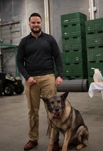 Military working dog, Morgen sits next to former handler dressed in civilian attire.
