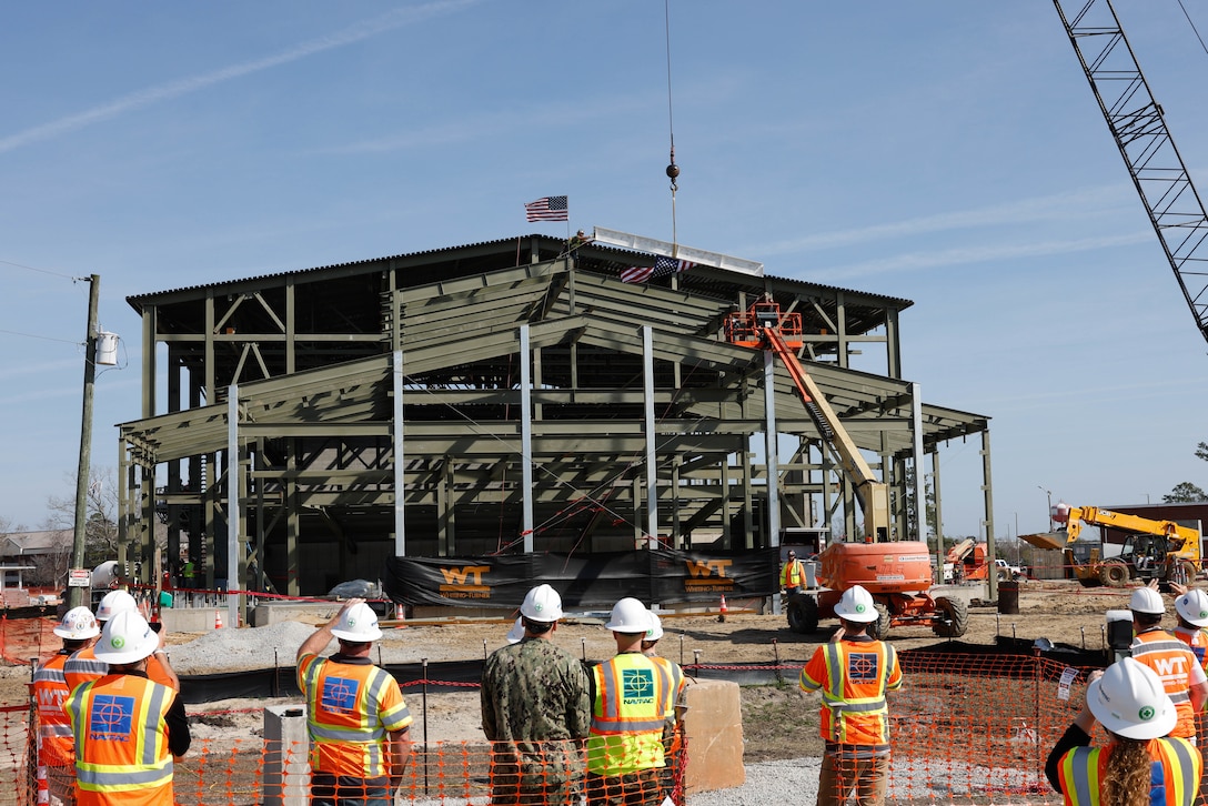 Attendees watch as the final beam is lifted to its place during the topping out ceremony for the future auditorium on Marine Corps Air Station (MCAS) Cherry Point, North Carolina, Feb. 22, 2023. The auditorium is part of the construction to rebuild and modernize structures damaged by Hurricane Florence. The topping out ceremony is a celebration of the facility structure being completed and the next stage of construction beginning. (U.S. Marine Corps photo by Lance Cpl. Lauralle Walker)