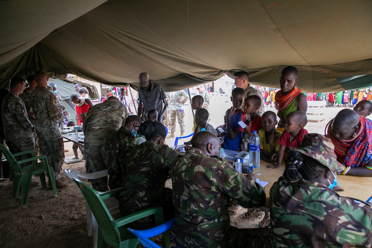 U.S. and African service members sit and stand behind a long table as other people stand on the other side.