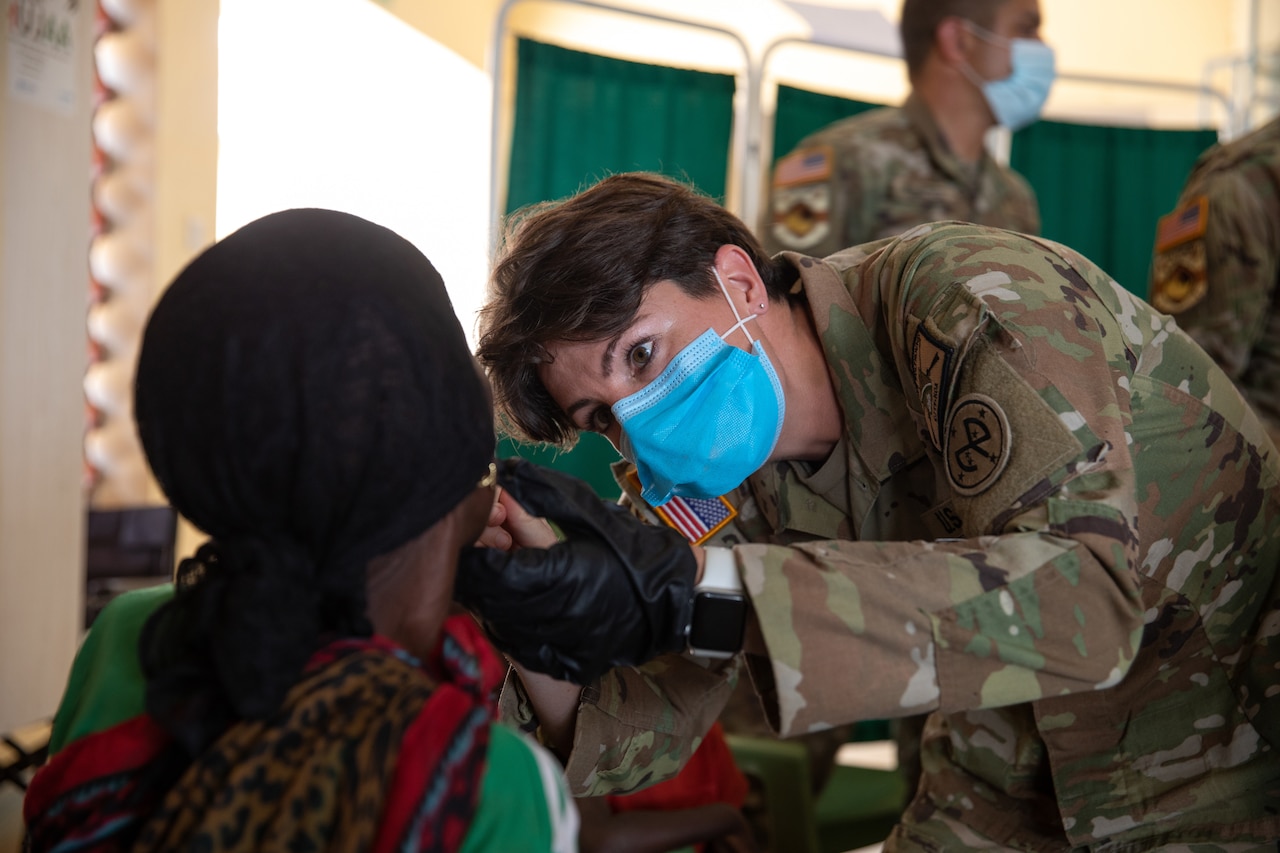 A soldier looks into the mouth of a patient.