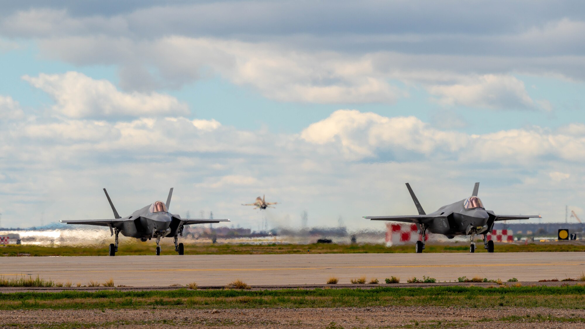 An F-16 Fighting Falcon takes off while two F-35A Lightning II aircraft idle on the runway, March 2, 2023, at Luke Air Force Base, Arizona.