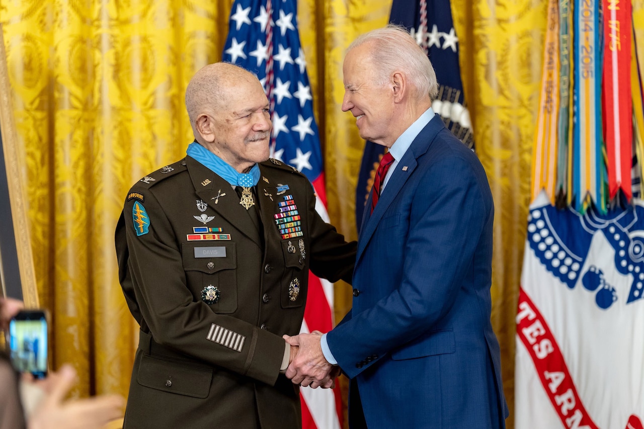 President Joe Biden shakes hands with a retired soldier in uniform wearing a Medal of Honor.