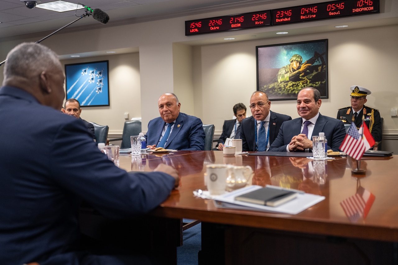 Several men in suits sit around a large wooden conference table.