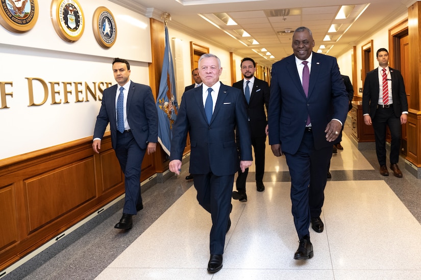 Several men wearing suits walk down a hallway together.