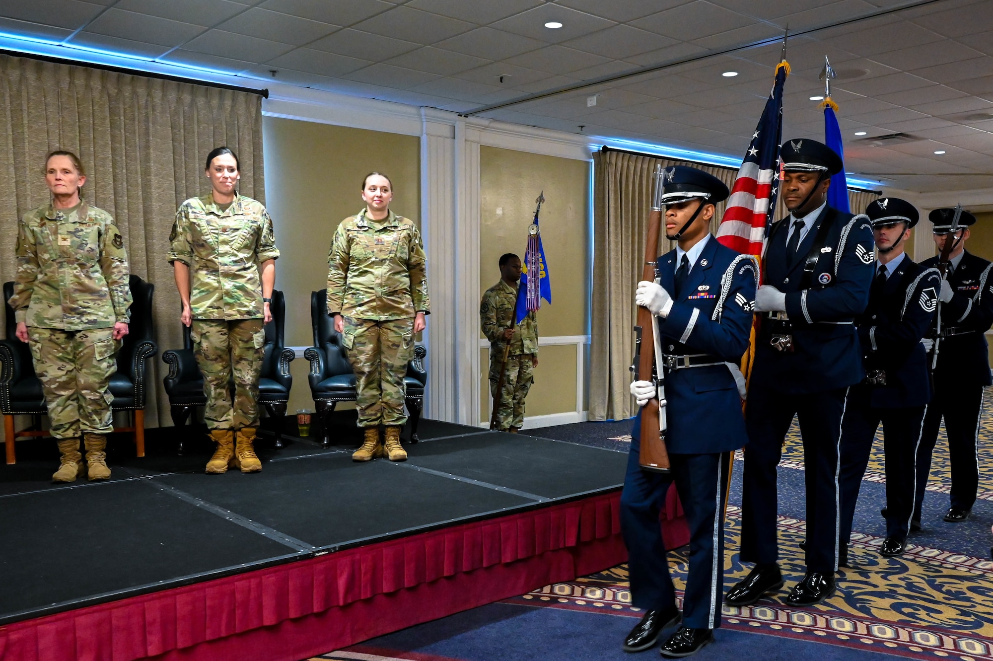 airmen standing at attention while other airmen carry the USA flag