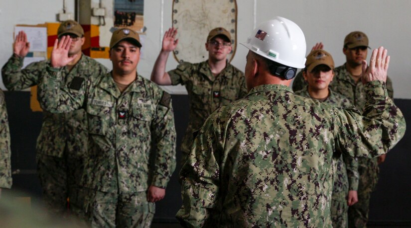 Sailors raise their right hands during a ceremony.
