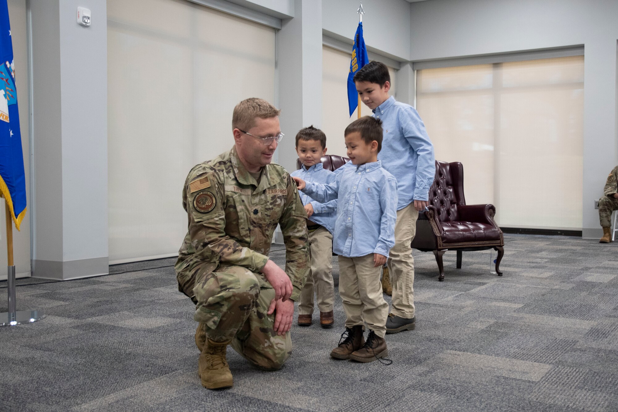 A man kneels while his children place a patch on his uniform.