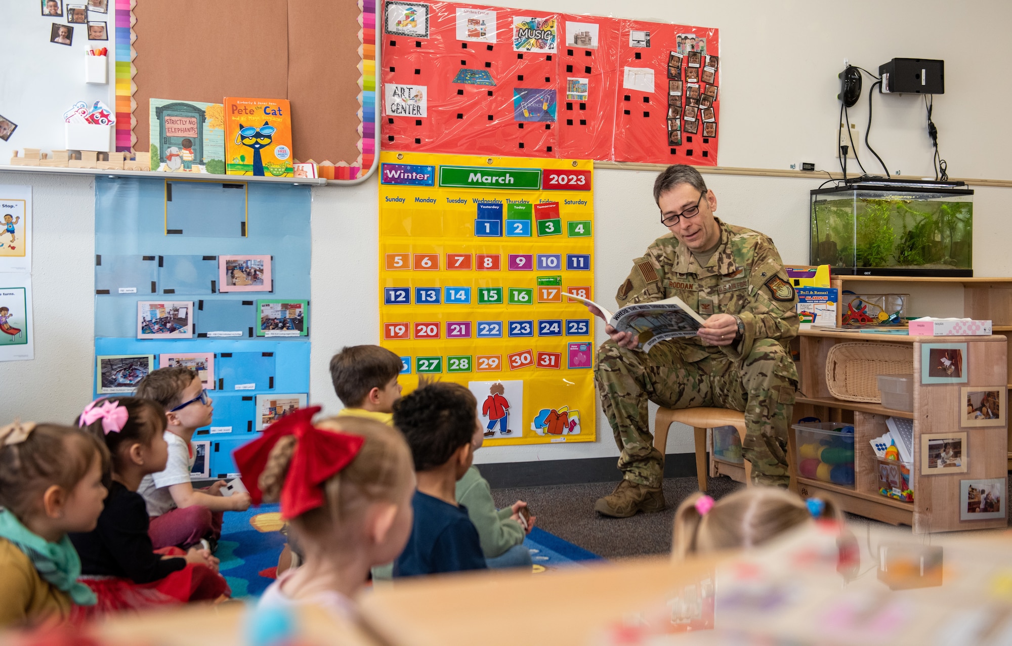 Military member in uniform reads to a group of children sitting on the floor