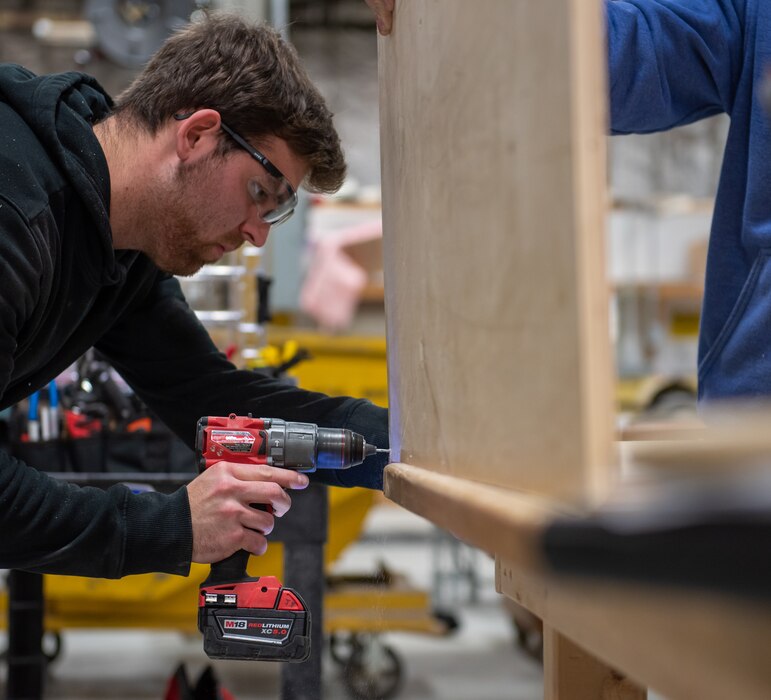 Jake Fletcher, 88th Civil Engineer Squadron carpenter, drills a screw into a piece of plywood to build a storage cabinet at Wright-Patterson Air Force Base, Ohio, Feb. 16, 2023. Fletcher has worked at Wright-Patt for nearly four years after beginning his career as a 17-year-old apprentice while attending Miami Valley Career Technology Center's construction carpentry program. (U.S. Air Force photo by Matthew Clouse)