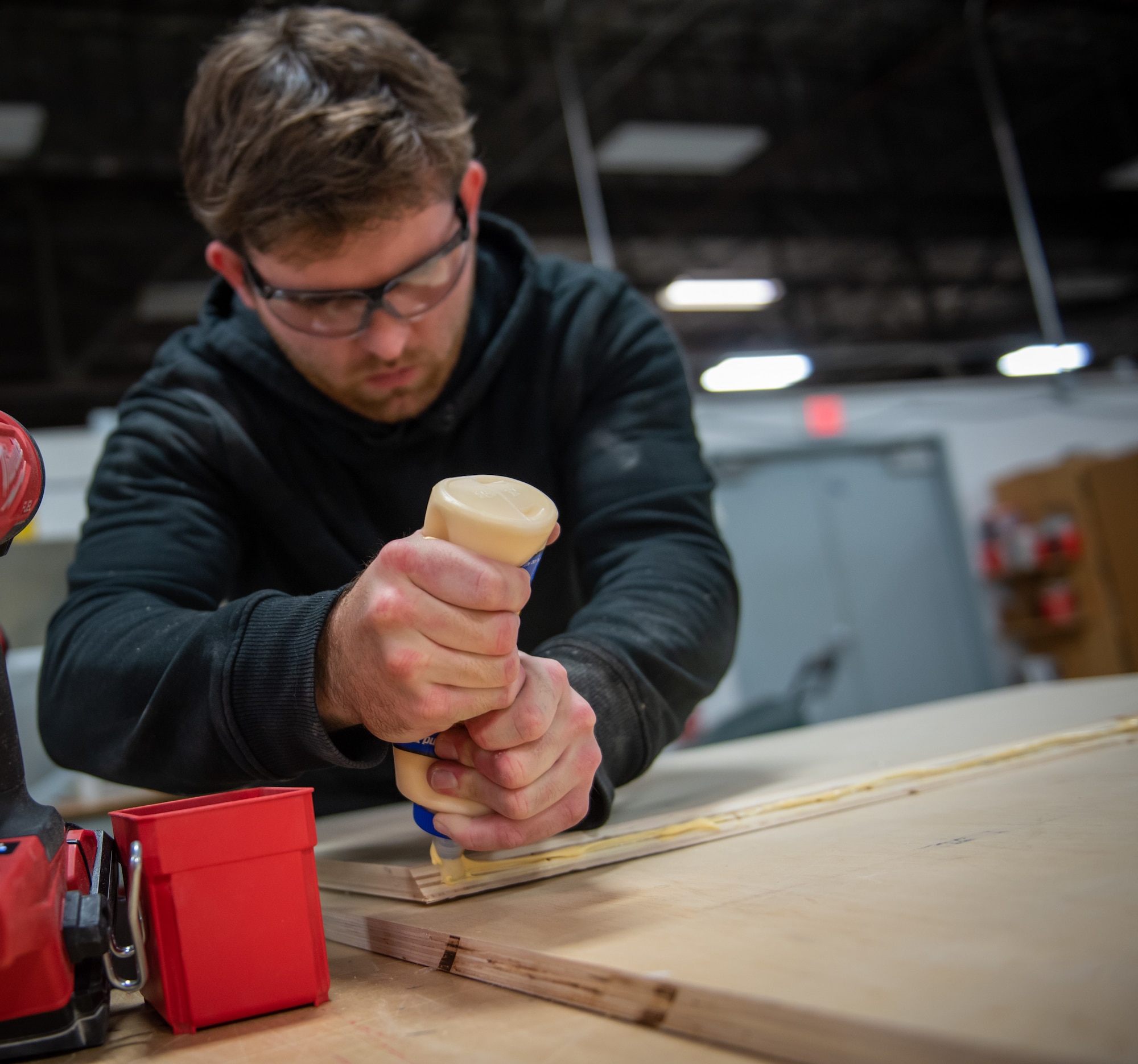 Jake Fletcher, 88th Civil Engineer Squadron carpenter, squeezes glue on a piece of plywood to build a storage cabinet at Wright-Patterson Air Force Base, Ohio, Feb. 16, 2023. Fletcher has worked at Wright-Patt for nearly four years after beginning his career as a 17-year-old apprentice while attending Miami Valley Career Technology Center's construction carpentry program. (U.S. Air Force photo by Matthew Clouse)