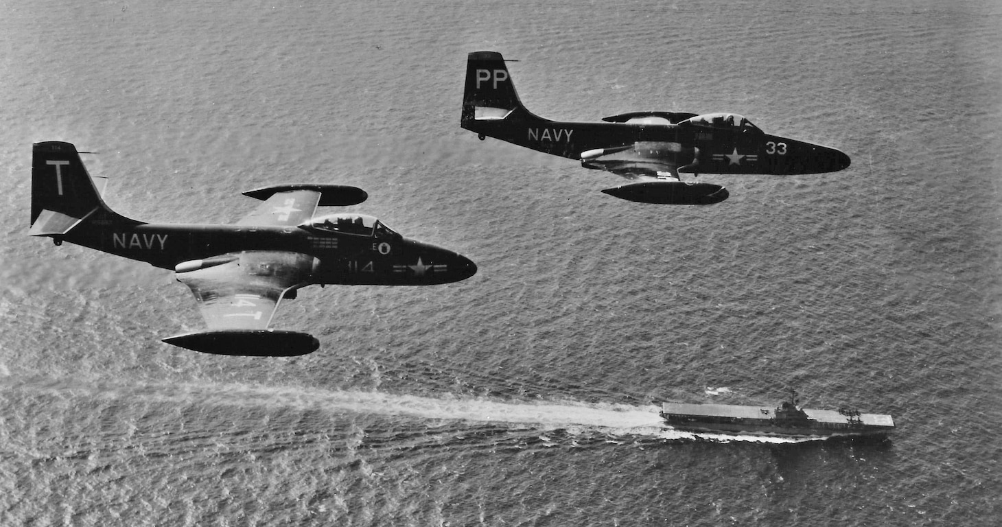 An F2H-2 (left) and an F2H-2P photo bird fly over the USS Kearsarge (CVA 33) during a 1952 combat deployment in Korea.