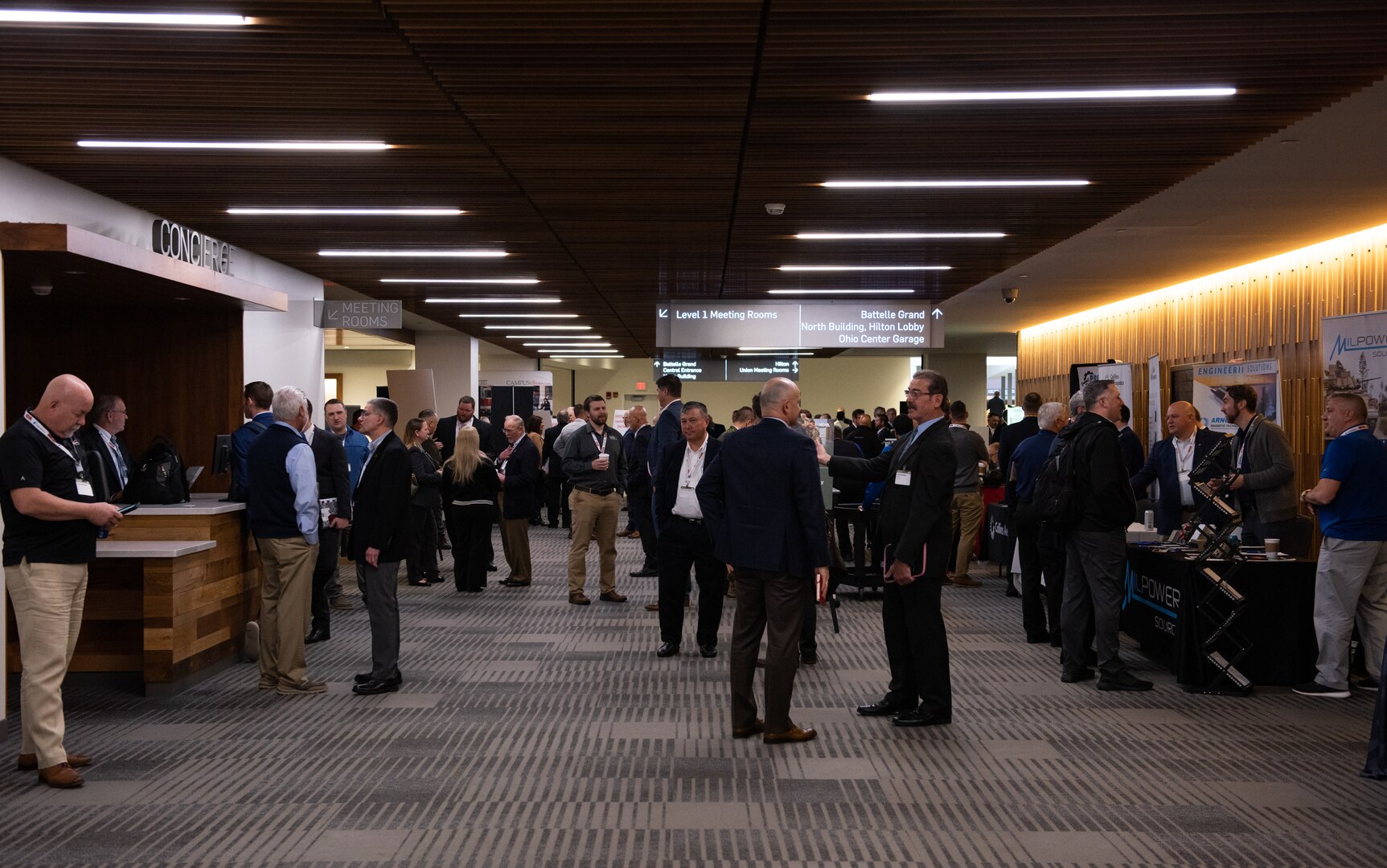 Many people in business dress visit booths in the hallway outside of a ballroom.