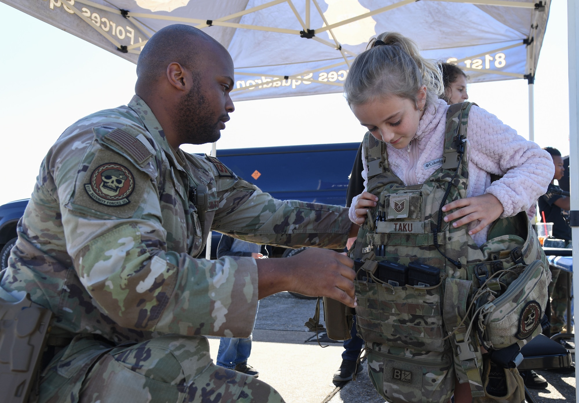U.S. Air Force Tech. Sgt. Michael Taku, 81st Security Forces Squadron flight sergeant, secures an individual ballistic armor vest on Harper Prentice, daughter of Capt. Heather Prentice, 81st Operational Medical Readiness Squadron family advocacy officer, during Operation Hero at Keesler Air Force Base, Mississippi, March 4, 2023.